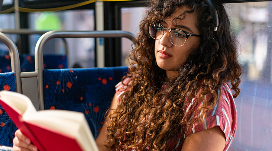 Young lady wearing reading glasses reading a book while riding the bus